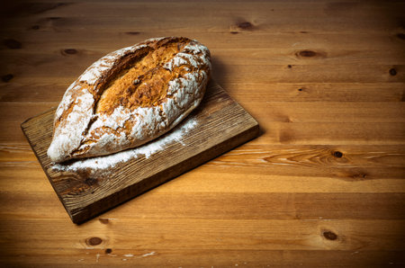 Loaf of bread on brown wooden cutting board against brown table