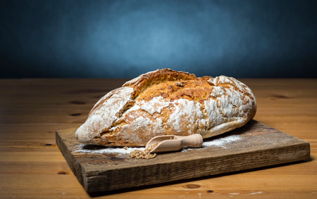 Loaf of bread on wooden cutting board and black background.