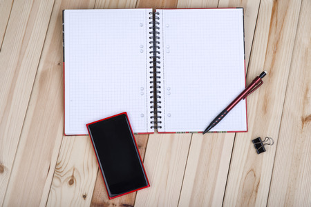 Red Smart Phone With Blank Black Screen, Notepad And Pencil On Wooden Desk.の写真素材