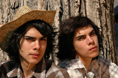 Two identical twins sitting outdoors under a tree
