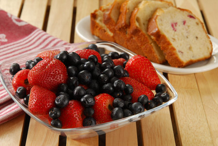 A bowl of strawberries nad blueberries and sliced cranberry bread