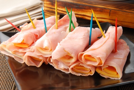 Rolled slices of ham and cheddar cheese for appetizersの写真素材