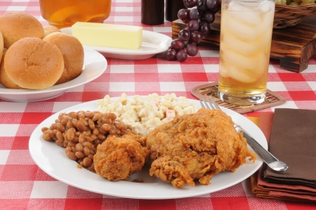 A plate of fried chicken with Boston baked beans and rolls on a picnic table on a summer dayの写真素材