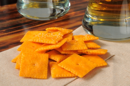A handful of cheese crackers on a cocktail napkin with glasses of beer on a bar counterの写真素材