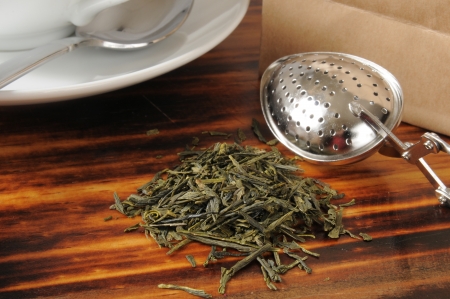 Whole leaf green tea on a counter with a tea infuser and the bag it cameout ofの写真素材