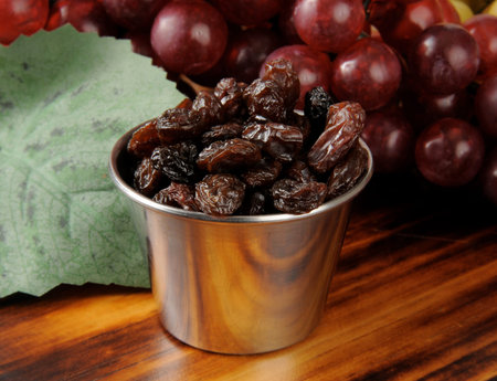 Fresh sun dried raisins in a silver snack dish with grapes の写真素材