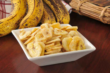 a bowl of dried banana chips on a wooden tableの写真素材