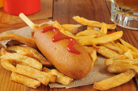 a corn dog and french fries with beer on a rustic wooden bar counter