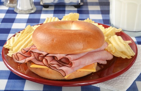 A ham and cheese sandwich on a bagel with a glass of milkの写真素材
