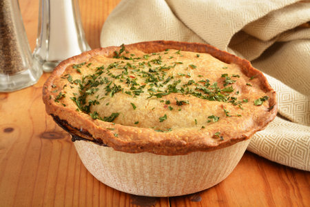 A gourmet pot pie topped with parsley on a rustic wooden table