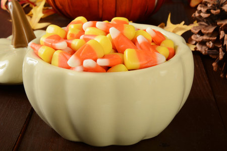 A pumpkin shaped dish of candy corn on a Halloween or Thanksgiving dinner table