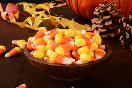 A wooden bowl of candy corn on a halloween table with a decorative pumpkinの写真素材