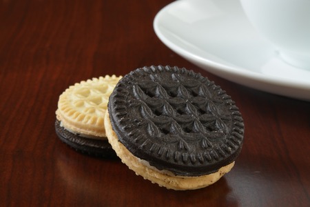 Cream filled vanilla and chocolate sandwich cookies with coffeeの写真素材