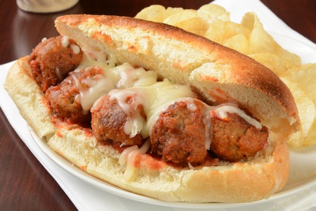 A meatball sandwich with mozzarella cheese and potato chipsの写真素材