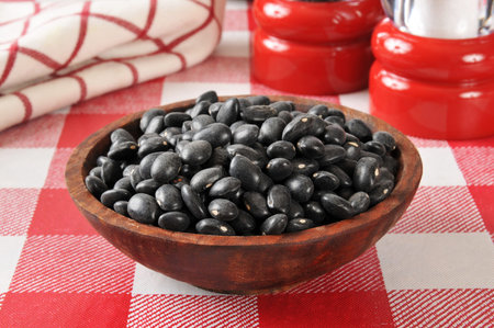A wooden bowl of black turtle beans on a colorful table