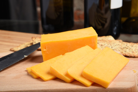 Closeup of slices of cheddar cheese with wine and crackers, shallow DOF focus near frontの写真素材