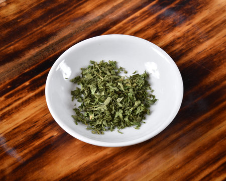 Dried parsley flakes in a small bowl on a cutting boardの写真素材
