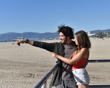 A happy young couple at the beach pointing at something in the distanceの写真素材
