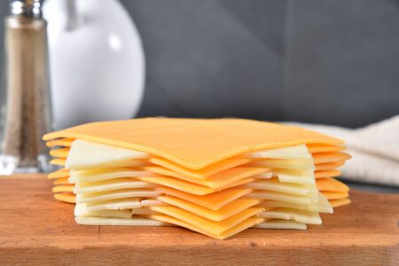 Slices of cheddar and Swiss cheese stacked on a cutting boardの写真素材