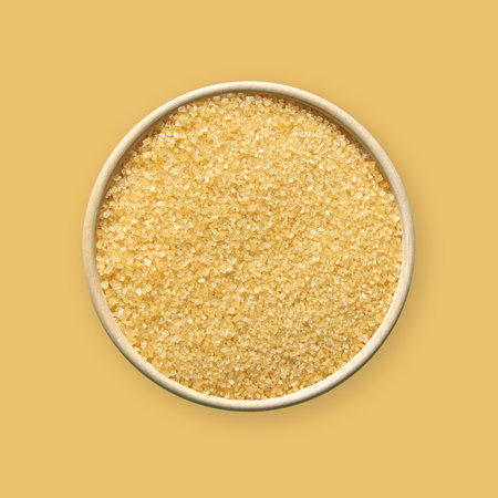 Brown cane sugar in bowl isolated on yellow background. Top view.の写真素材