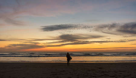 Surfing sunset. Silhouette of female surfer carrying boards along the sand of a beachの写真素材