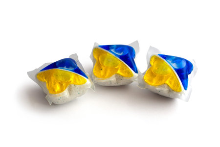 Three blue and yellow dishwasher tablets on isolated white background