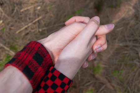 Punk emo couple holding hands, wearing red checkered armband while walking outdoors in the forest, close-upの写真素材
