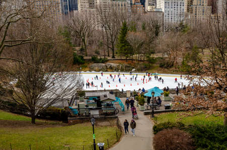 Wollman Rink with People Ice Skating during daytime in winter, view from the distance, Central Park New York City, benches and people walking in the forefront, horizontalのeditorial素材