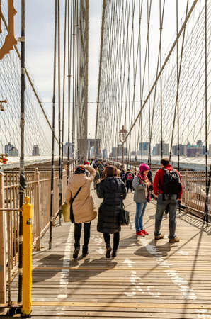 People walking and standing on Brooklyn Bridge during sunset, New York City, construction area on bridge, verticalのeditorial素材