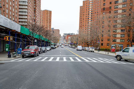 Residential Area with old brown apartment skyscraper buildings, City street with crosswalk and traffic in Harlem, New York City, during winter day with overcast, horizontalのeditorial素材