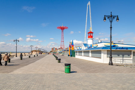 Red Parachute Jump of Luna Park Amusement Park with Beach Promenade in front, People walking, Street lights and green trash cans in a row, Coney island, Brooklyn, New York City during winter day with clear sky, wide angle, horizontalのeditorial素材