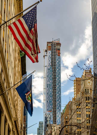 Park Hyatt Skyscraper Construction Site at W57th ST, New York City with American flag in the front, view from low angle during sunny winter day with cloudy sky, verticalのeditorial素材