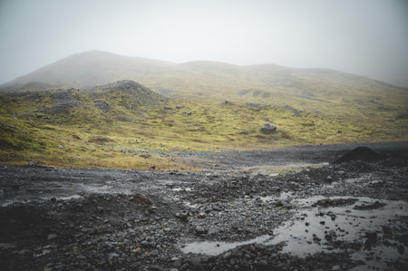 Landscape of iceland with black stones and sand at the bottom and green overgrown mountain range in the distance, perfect backgroundの写真素材