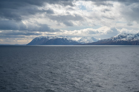 Iceland snow mountains with sea in front background during cloudy weather, view from the distance,...