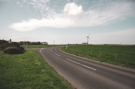Road at the countryside of Kirkwall, Scotland with residential building and modern wind turbine on the horizonの写真素材