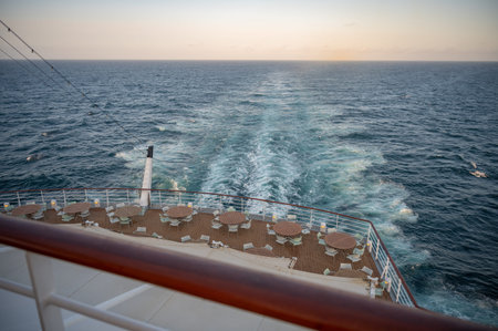Round tables and chairs standing on boat deck at the back side of a cruise ship during sunset, sea...