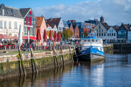 Husum harbor district during autumn with lots of tourist in the city, colorful building facades, blue ship with river in front, horizontal shotの写真素材
