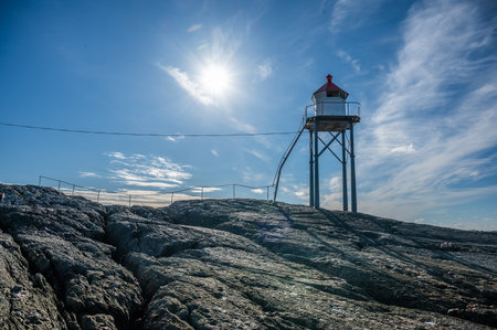Kvalen fyr lighthouse stands on rocky terrain under a bright sun, with a clear blue sky and scattered clouds, Haugesund, Norwayの写真素材