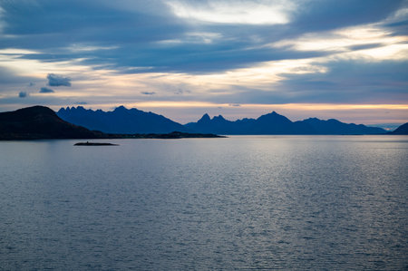 A serene seascape at dawn features a calm body of water with distant mountains and a solitary island, under a soft, colorful sky.の写真素材