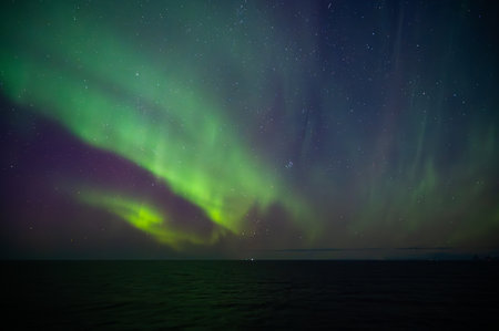 A mesmerizing display of the Northern Lights illuminates the night sky over a calm sea, creating a breathtaking visual spectacleの写真素材