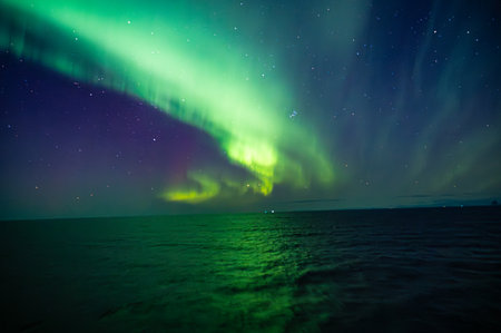 A mesmerizing display of the Northern Lights illuminates the night sky over the ocean, creating a breathtaking and serene sceneの写真素材