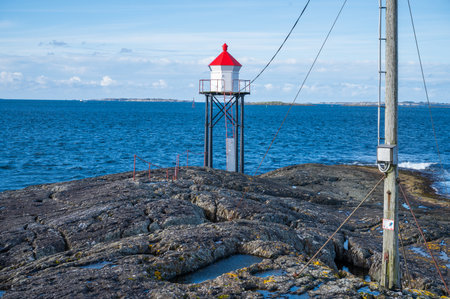 Kvalen fyr, a red-roofed lighthouse stands on a rocky outcrop by the sea, with a distant island and a clear sky in the background, Haugesund, Norwayの写真素材
