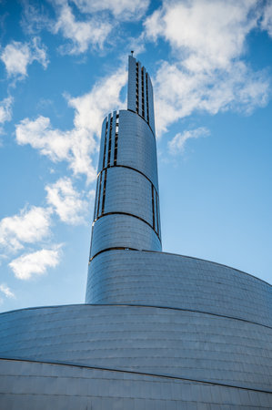 Northern Lights Cathedral, Alta, a modern, cylindrical tower with a sleek, metallic design rises against a blue sky with scattered clouds, vertical shot, Norwayの写真素材