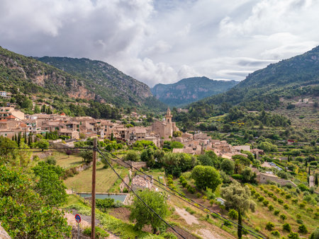 Valldemossa, Mallorca, picturesque village nestled in a valley surrounded by lush green hills and a cloudy sky, with a prominent tower standing out in the center, wide angle shot, Majorcaの写真素材