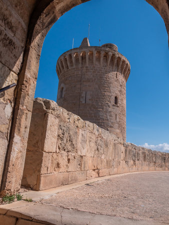 Bellver Castle. Palma de Mallorca, historic stone tower stands under a clear blue sky, framed by an ancient stone archway, Majorcaの写真素材