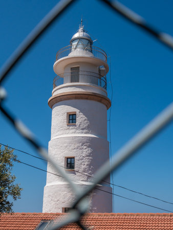 Far del Cap Gros, Mallorca lighthouse Port de Soller, with a white cylindrical tower and a metal railing stands under a clear blue sky, viewed through a chain-link fence, Majorcaの写真素材