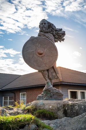 King Harald, Fairhair statue, bearded warrior holding a shield stands in front of a house with a cloudy sky, sunbeam, vertical shot, Haugesund, Norwayの写真素材
