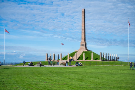 Haraldshaugen, Haugesund, Norway, monument with a tall obelisk stands in a grassy field, surrounded by flagpoles, with people sitting and walking aroundの写真素材
