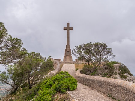 Santuari de Sant Salvador, Mallorca, stone cross stands atop a hill, surrounded by greenery under a cloudy sky, Majorcaの写真素材