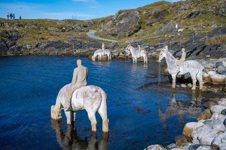 The Rising Tide, Haugesund, Norway, serene landscape features a person on a horse drinking from a tranquil body of water, surrounded by statues of horses and people, with a path and distant figures in the backgroundの写真素材